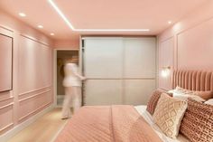 a woman walking into a bedroom with pink walls