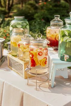 several jars filled with water and lemons on a table outside in front of some bushes