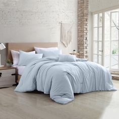 a bedroom with white brick walls and wooden flooring has a large bed covered in beige linens