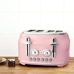 a pink toaster sitting on top of a wooden counter next to a plate of food