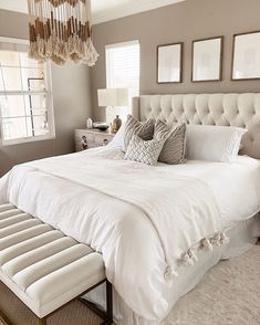 a large white bed sitting in a bedroom next to a window with pictures on the wall