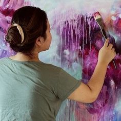 a woman is painting on the wall with purple paint