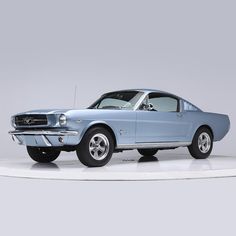 an old blue mustang muscle car sitting on top of a white stand in front of a gray wall