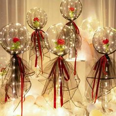 four clear vases with red roses and lights on them are sitting in front of a window