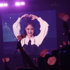 a woman standing on top of a stage holding her hands up in the air while wearing a white shirt and black tie