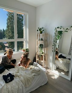 two women sitting on a bed in front of a large window