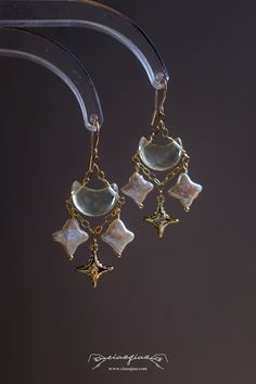 ---- Welcome to CiaoQiao Shop ----- Illuminate your style with the ethereal beauty of our "Enchanted Celestial Charm Earrings." Carefully crafted to capture the whimsical allure of a starry night, these earrings feature genuine baroque pearls fashioned into delicate stars, each one unique in its luster and form. Dangling gracefully from a chain of gold, they accompany a golden crescent moon, creating a celestial dance of elegance and charm. The stars and moon are suspended from a fine gold-tone Porcelain Hand Jewelry, Dangle Earring Display, Celestial Diamond Jewelry, Fancy Jewellery Earrings, Whimsical Earrings, Upcycled Earrings, Ethereal Jewelry, Stars Earrings, Whimsical Accessories