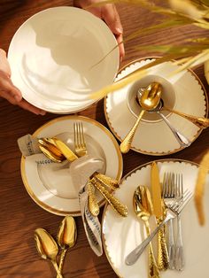 a table topped with white plates and gold colored utensils next to silverware