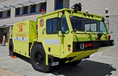 a bright yellow fire truck parked in front of a building with people walking around it