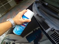 a person is holding a spray bottle near the hood of a car with its hood open