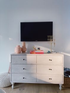 a tv mounted on the wall above a dresser in a room with white walls and wooden floors