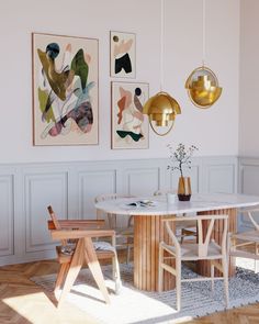 a dining room with white walls and wooden floors, artwork on the wall above the table