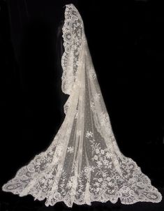 the back of a wedding veil with white flowers and lace on it, against a black background