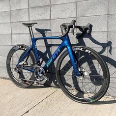 a blue bike leaning against a wall with its shadow on the ground next to it