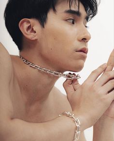 a shirtless young man wearing a chain around his neck and hand on his chest