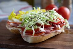 a sandwich with meat, lettuce and tomatoes on it sitting on a cutting board