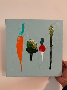 a person holding up a piece of art with vegetables painted on it's sides