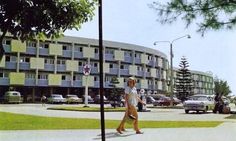 a woman walking down the street in front of a large building with balconies