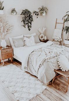 a bed with white sheets and pillows in a bedroom next to two potted plants