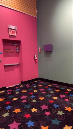 an empty room with pink walls and colorful stars on the floor in front of a paper dispenser