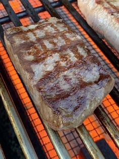 two steaks cooking on an outdoor grill