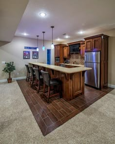 a kitchen with an island and bar stools in the center, surrounded by brown tile flooring