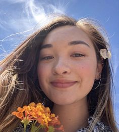 a girl with flowers in her hair smiles at the camera, against a blue sky