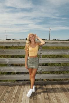 a woman standing on top of a wooden deck next to a fence with her hands behind her head