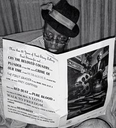 a young man reading a newspaper while wearing a hat