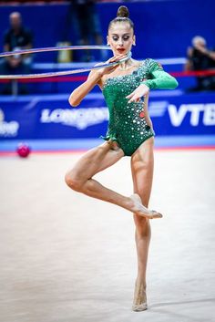 a woman in a green leotard doing a trick with a hula hoop