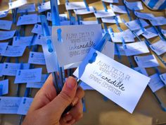 someone is holding up some blue and white business cards with writing on them that are attached to toothpicks