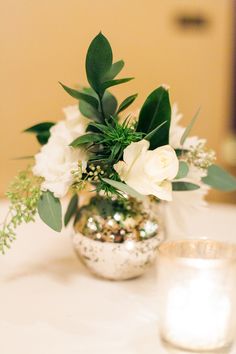 a vase filled with white flowers sitting on top of a table next to a candle