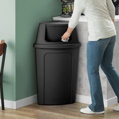 a woman standing next to a black trash can