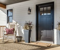 a porch with two chairs and potted plants next to the front door on a sunny day