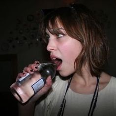 a woman drinking from a bottle while standing in a dark room with her mouth open