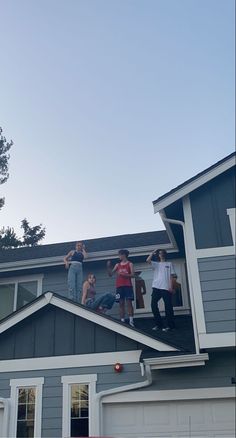 four people standing on the roof of a house with their hands up in the air