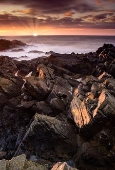 the sun is setting over some rocks by the ocean