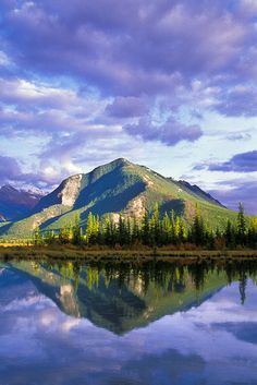 the mountains are reflected in the still water on the lake's edge, while the clouds loom above them