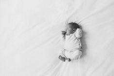 a black and white photo of a baby laying on a bed with its head up