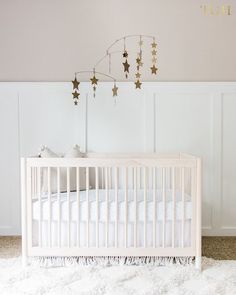 a white crib with gold stars hanging from it's ceiling and a rug on the floor