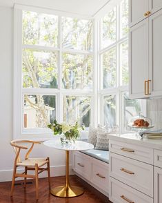 a kitchen with white cabinets and wooden flooring next to a window filled with lots of windows