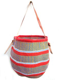 a red and blue striped basket hanging from a hook on a white wall next to a brown leather strap