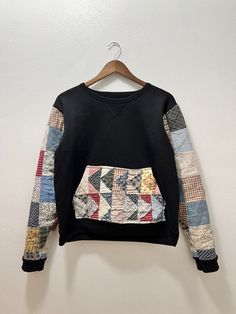 a black sweatshirt with multicolored patchwork on the front and back, hanging from a hanger