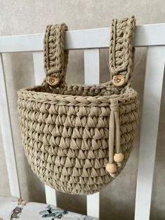 a woven bag hanging from the side of a white wooden chair next to a wall