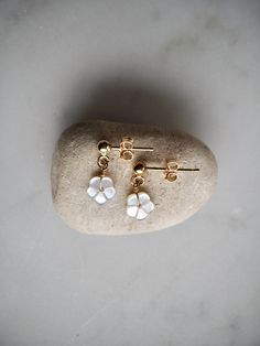 Delicate and dainty gold stud earrings with tiny white mother of pearl flower dangle. These sweet mop sakura flower stud earrings are lightweight and minimalist - the perfect everyday earrings.  14 k gold filled studs with 3mm ball. Comes with gold filled backs. The mop flower is 6mm.  Made using the highest quality USA and UK sourced materials. 📦 Eco-friendly packing I try my best to use as little plastic as possible in my packaging. Each order will arrive wrapped in a sweet eco-friendly and b Delicate White Teardrop Flower Earrings, White Teardrop Jewelry With Flower Charm, Dainty White Sterling Silver Bridal Earrings, Tiny White Sterling Silver Earrings, White Pearl Drop Dangle Cluster Earrings, Dainty White Dangle Bridal Earrings, White Pearl Drop Cluster Earrings, Tiny Delicate Gold Earrings, Delicate Teardrop Flower Earrings For Anniversary