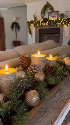 candles are sitting on a table with pine cones and evergreen greenery in front of the fireplace