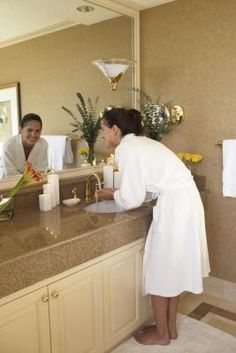 a woman in a bathrobe standing at a bathroom counter with flowers and candles