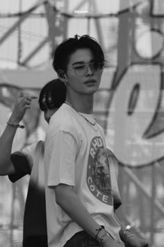 black and white photograph of a man with glasses on his head standing in front of a graffiti covered wall