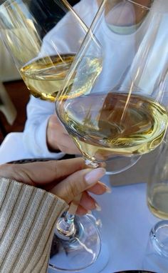 two people holding wine glasses with white wine in them