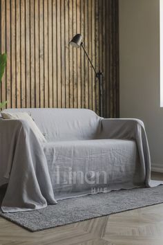 a couch covered with a blanket in front of a lamp and wooden wall behind it